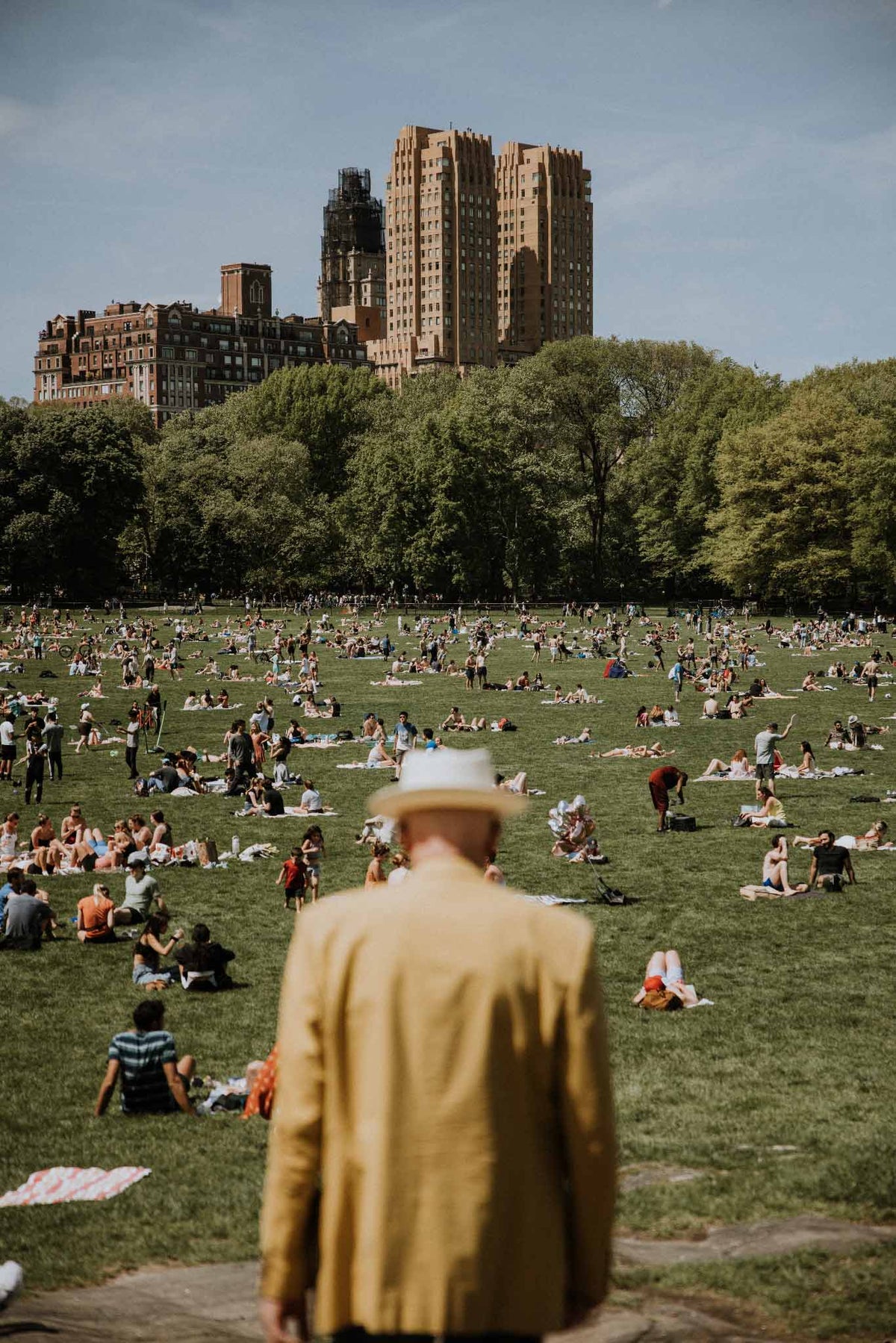 The Man in Yellow by Will Salkeld, a man in a yellow coat walking into a Spring scene on the Central Park Great Lawn, colour photography.
