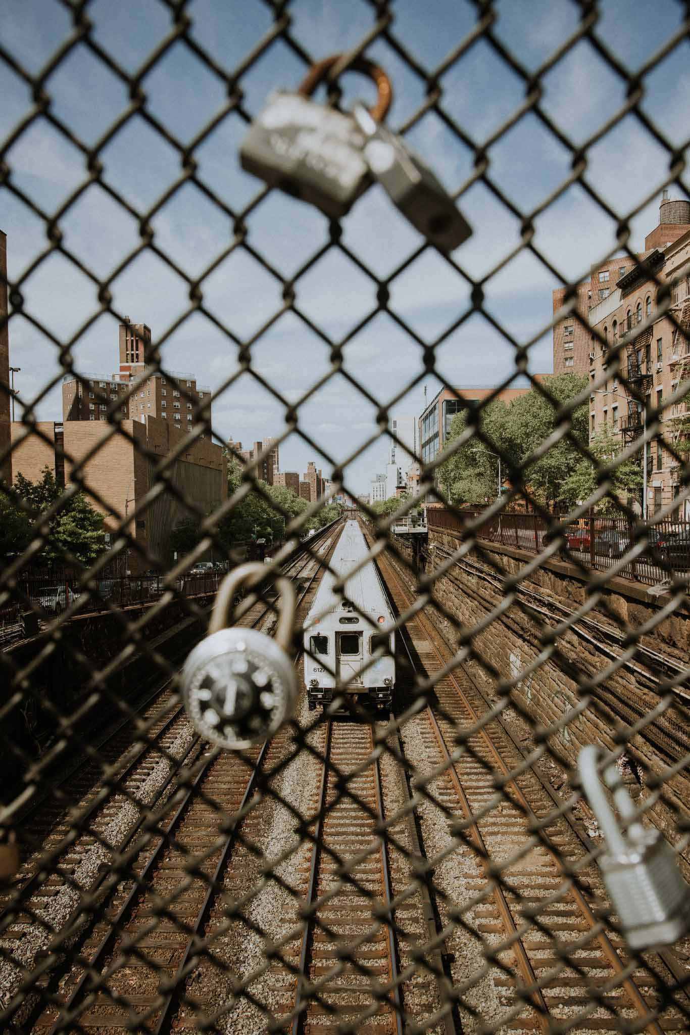 Locked In by Will Salkeld, a chain-link fence covered in padlocks above a Manhattan train line, colour photography.
