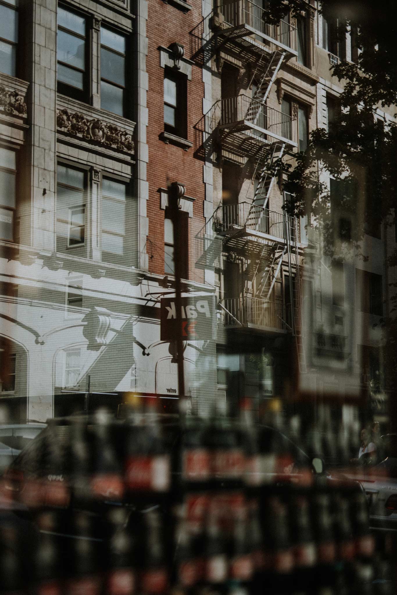 Cola by Will Salkeld, Manhattan fire escapes and brownstones reflected on a soda shop window with a vintage Coca-Cola display, colour photography.