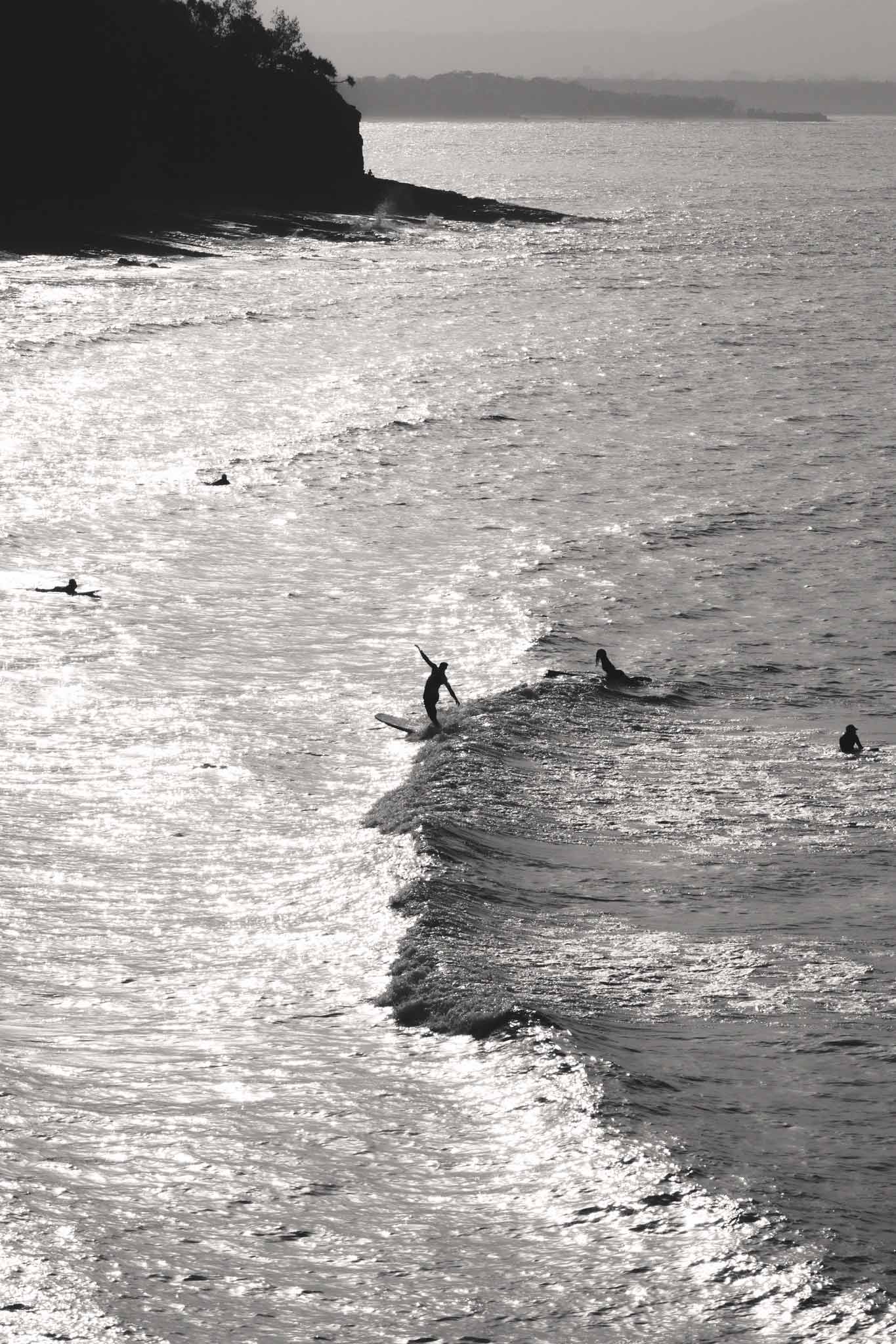 Surfers Wave by Raex Murillo, black and white photograph of a solo surfer poised on a wave against a shimmering Tamarama sea