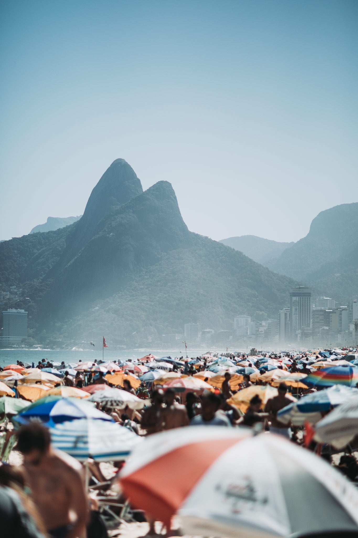 Dois Irmãos by Will Salkeld, crowded Ipanema beach with the twin peaks of Dois Irmãos rising behind, colour photography.